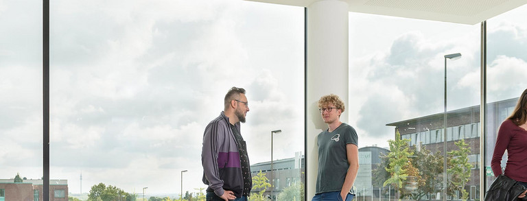 Studenten in Gesprächssituationen vor einer Fensterfront